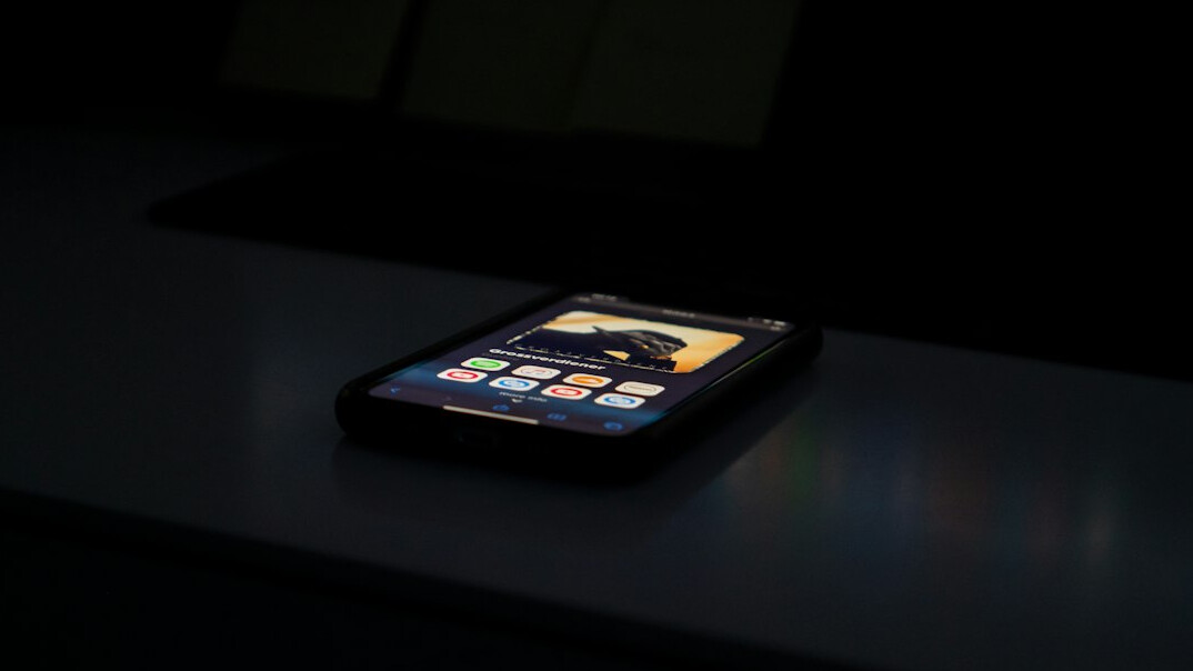Laptop and smartphone on a dark desk reflecting soft blue and amber screen light